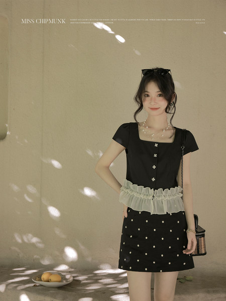 Black short-sleeve polka dot dress with white ruffle trim worn by a model