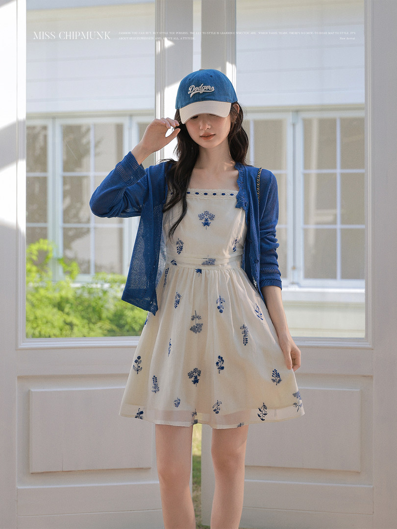 Woman wearing a cream floral dress with a blue cardigan and baseball cap