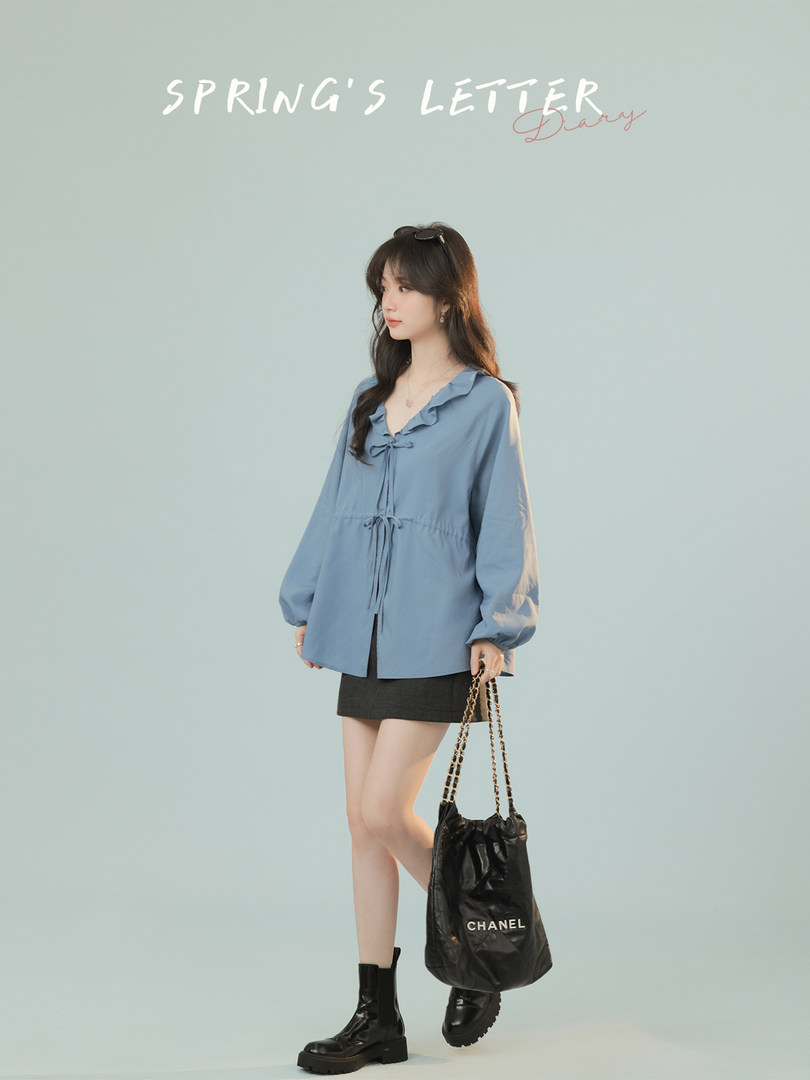 Model wearing a light blue ruffled blouse with a black skirt and black boots