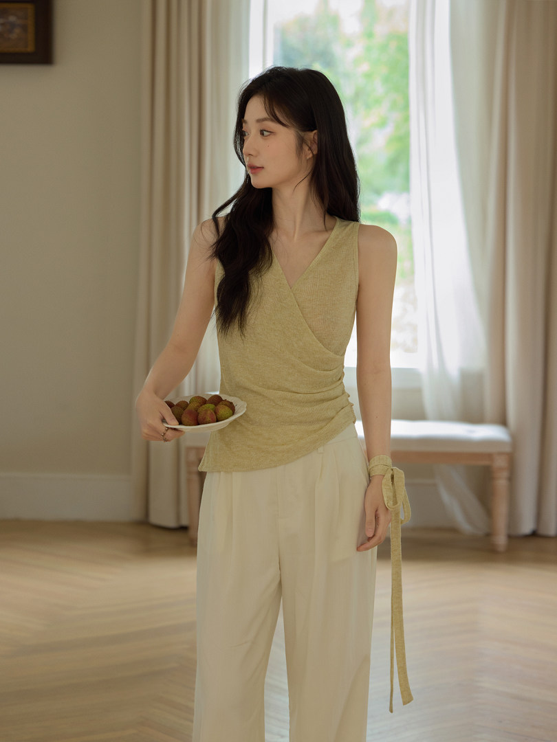 Woman wearing a light beige sleeveless wrap top with cream wide-leg pants indoors