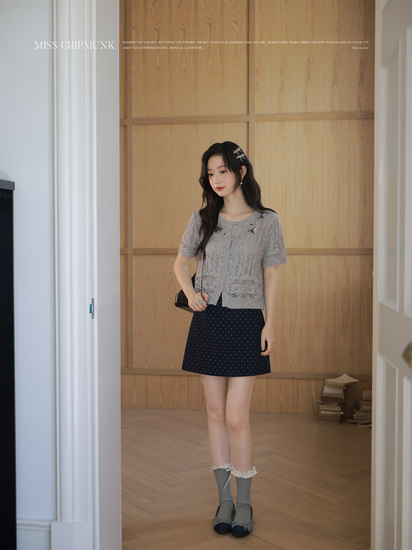 Model wearing a gray knit short-sleeve cardigan with a navy polka dot skirt