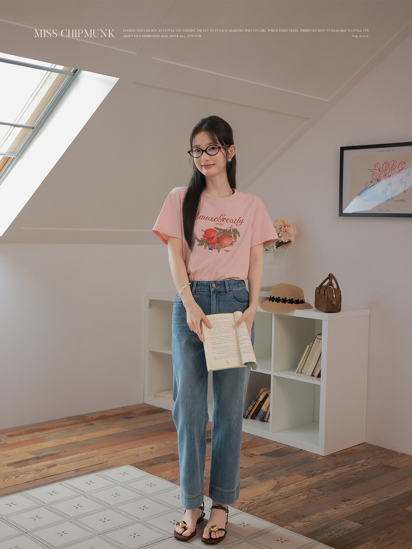 Woman wearing a pink graphic T-shirt and blue jeans indoors