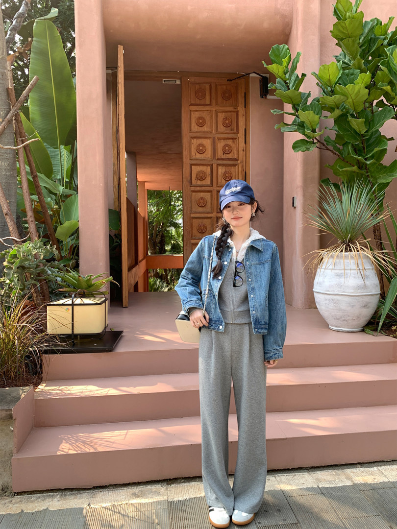 Woman wearing a grey sweatsuit with a denim jacket and cap outdoors