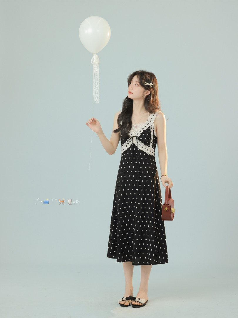 Model wearing a black polka dot sleeveless dress with white lace trim and a small handbag