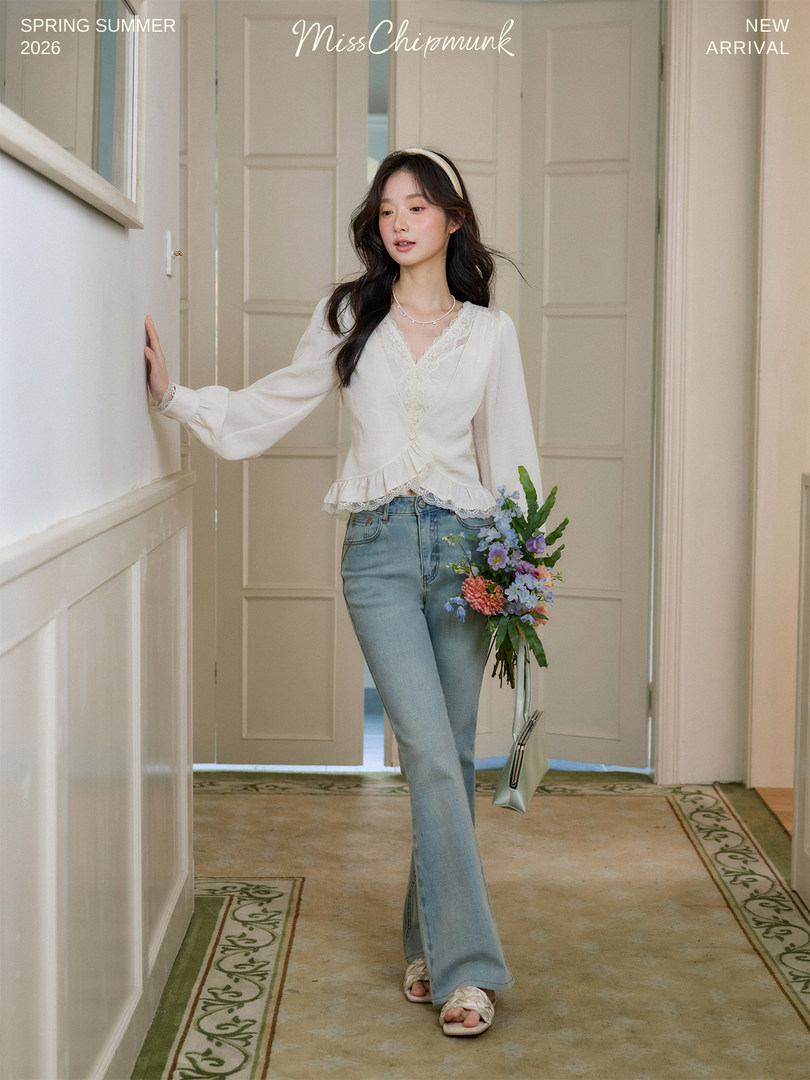 Young woman modeling a white lace blouse with light blue jeans in a soft indoor setting
