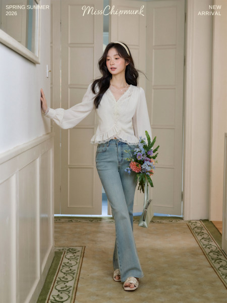 Young woman modeling a white lace blouse with light blue jeans in a soft indoor setting
