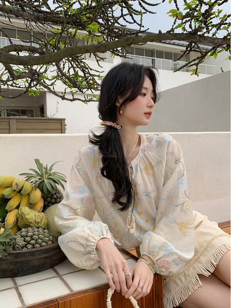 Woman wearing a light floral blouse and fringed skirt outdoors.