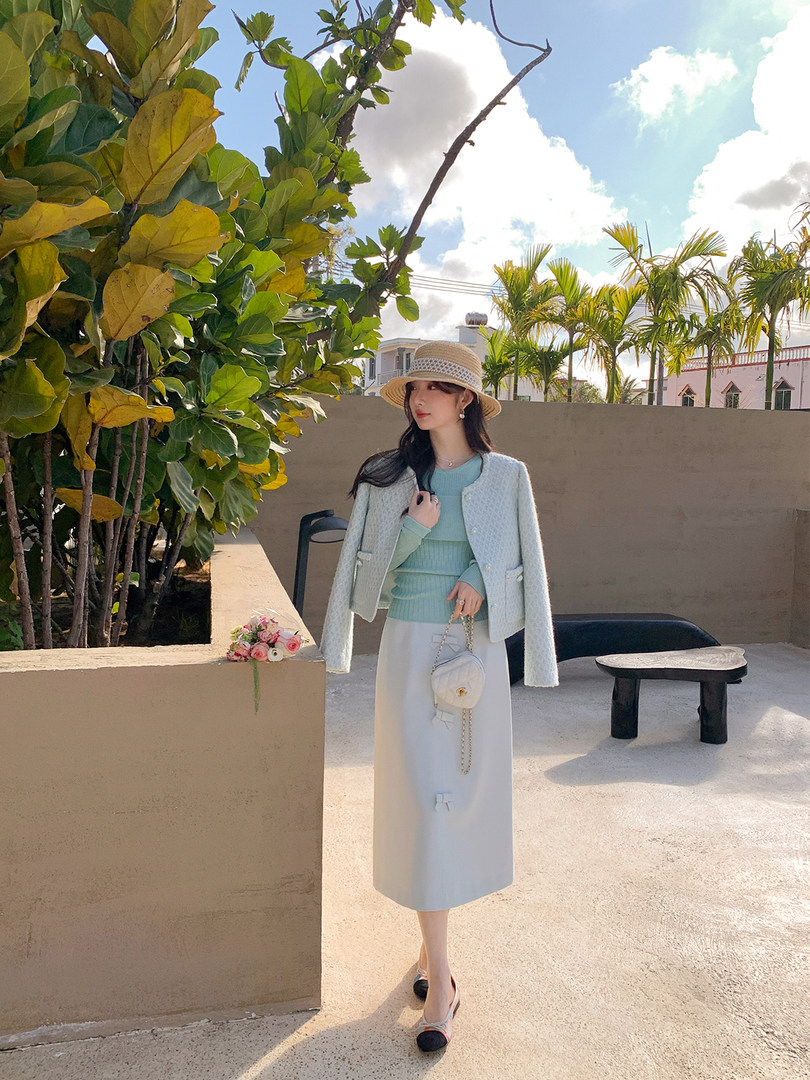 Woman wearing a light pastel outfit with a jacket, skirt, and hat outdoors