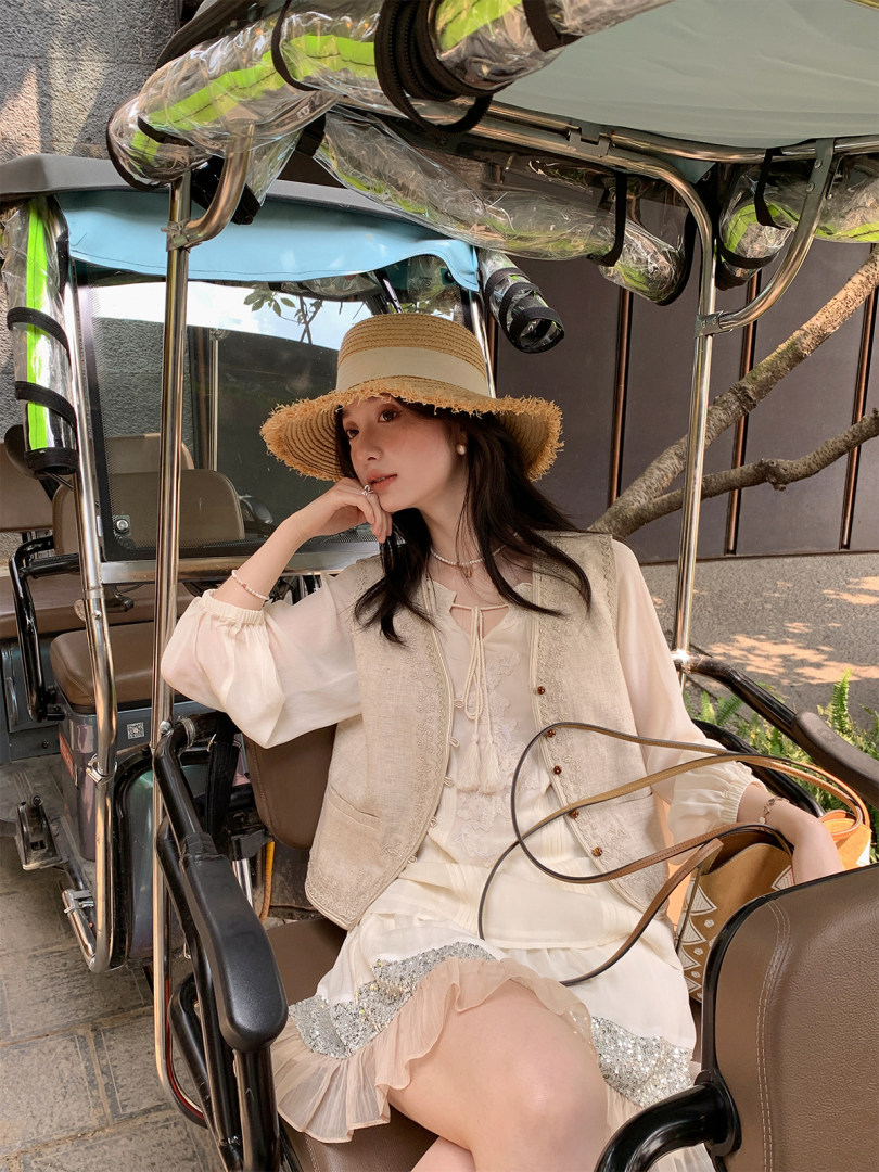 Woman wearing a light summer outfit with a straw hat and handbag while seated in a vehicle