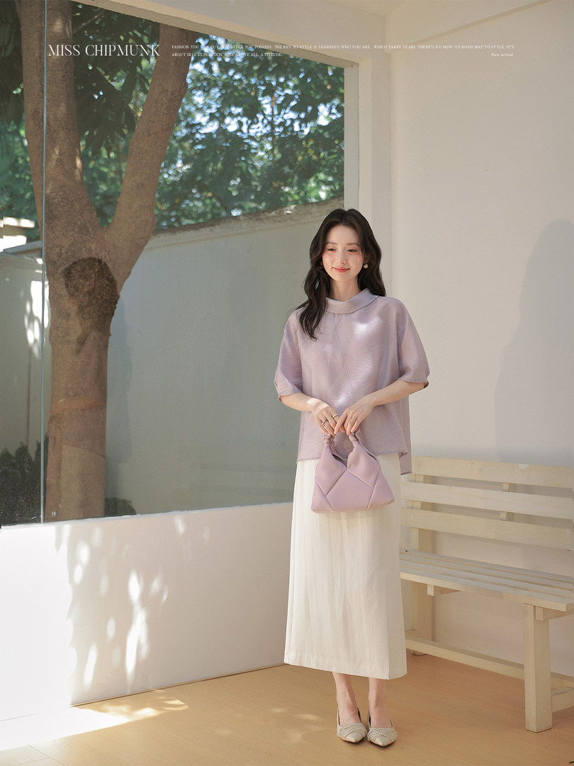 Woman wearing a light lavender blouse and white skirt holding a matching lilac handbag