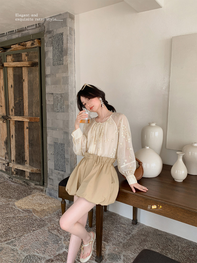 Woman wearing a cream lace blouse with a beige high-waisted skirt in a styled indoor setting