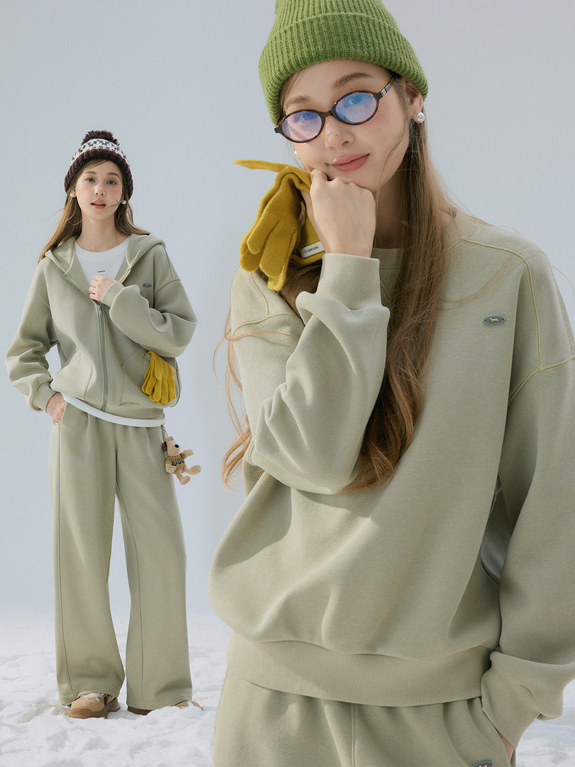 Model wearing a light green sweatshirt and matching wide-leg pants with knit beanie and gloves in a snowy setting