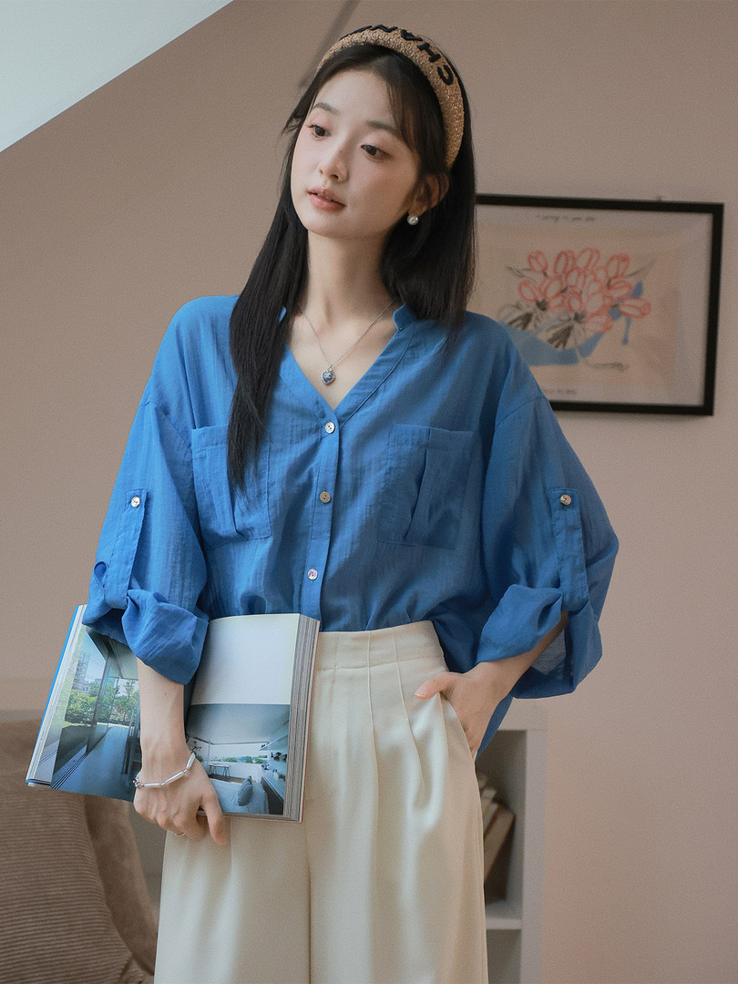 Model wearing a loose blue button-up blouse with cream pants