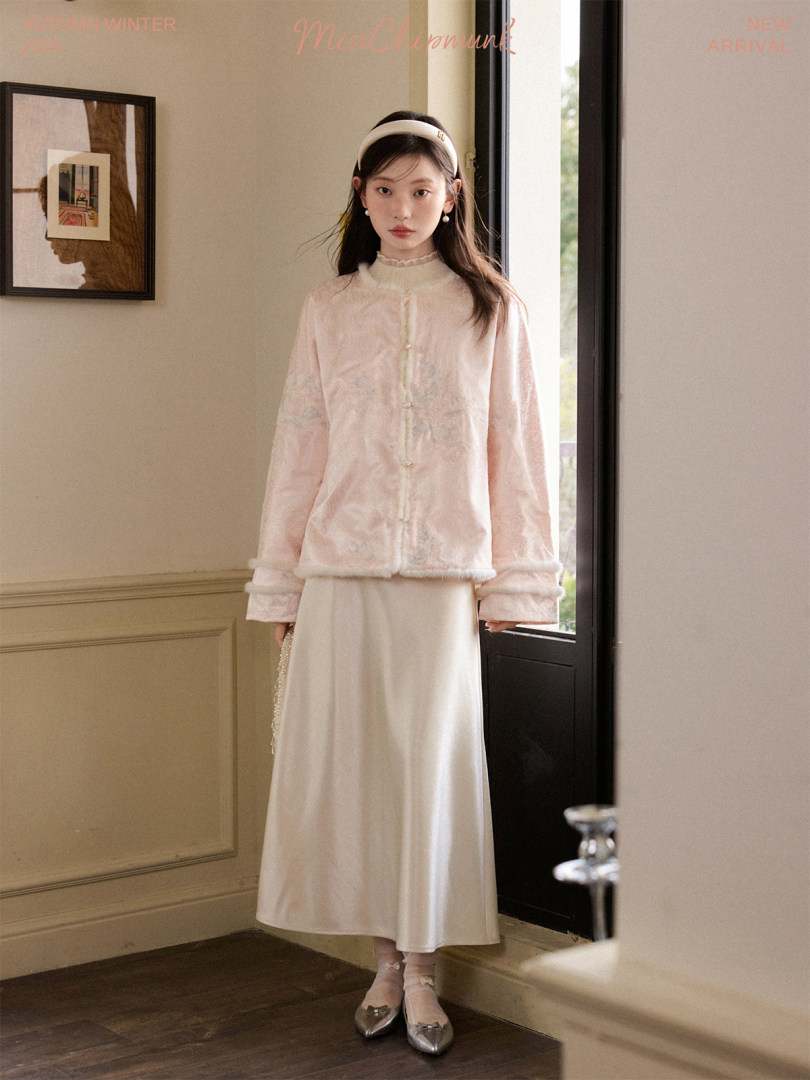 Model wearing a pale pink cardigan and cream satin skirt in an indoor fashion photo