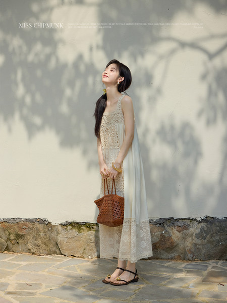 Woman wearing a cream lace maxi dress and holding a woven bag outdoors