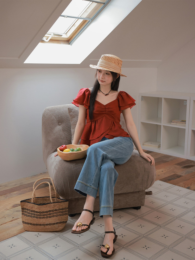 Woman modeling a red puff-sleeve top with blue jeans, straw hat, sandals, and woven tote bag
