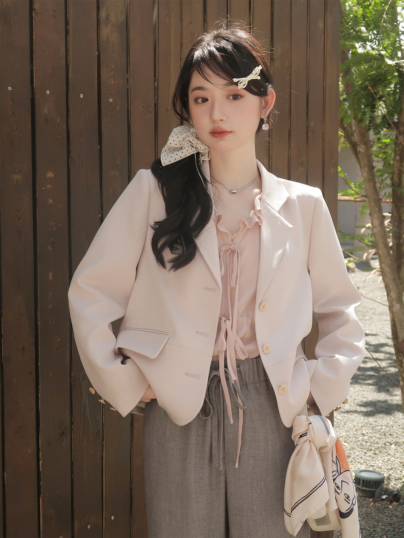 Woman wearing a light pastel blazer with a pink ruffled blouse and gray trousers