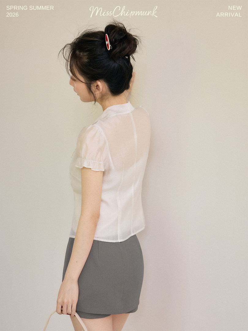 Model wearing a sheer white short-sleeve blouse with gray shorts