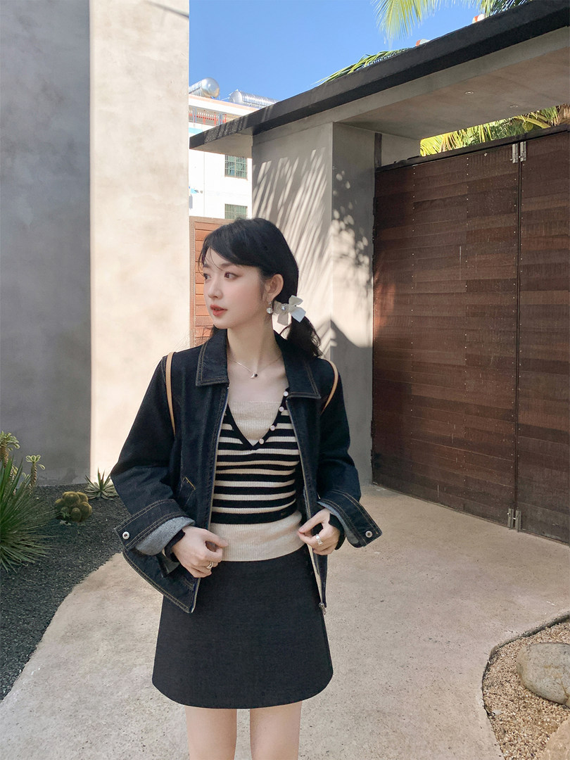Woman wearing a black denim jacket over a striped top with a black skirt outdoors