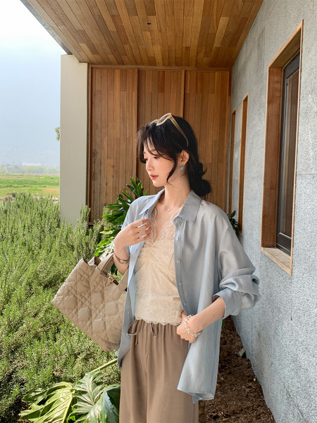 Woman modeling a light blue overshirt with a lace camisole, wide-leg pants, and a quilted beige tote bag