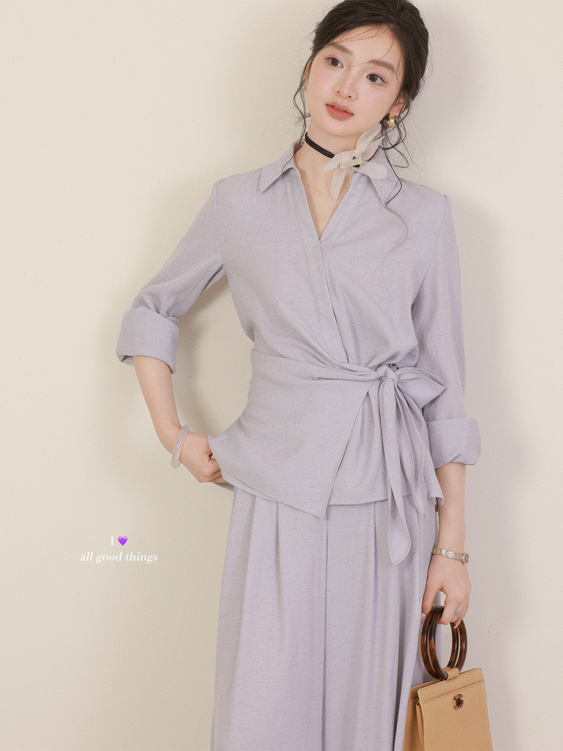 Woman wearing a light lavender belted dress with rolled sleeves and a tie waist