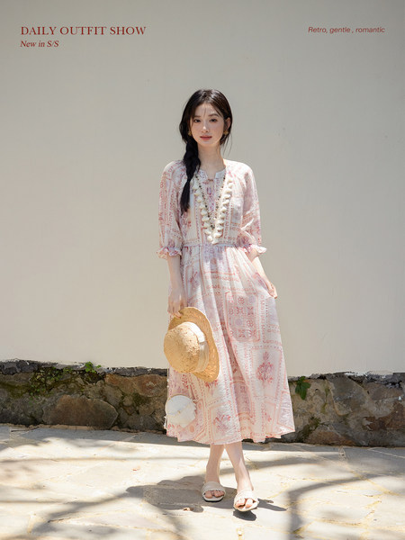 Model wearing a light pink patterned midi dress with a straw hat and sandals