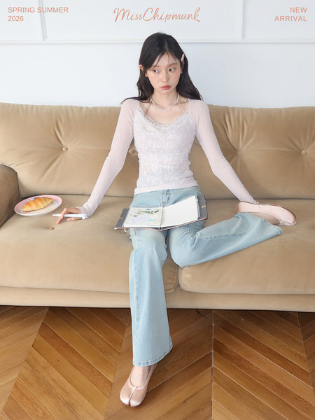 Model wearing a white long-sleeve top with light blue jeans and pink flats on a sofa