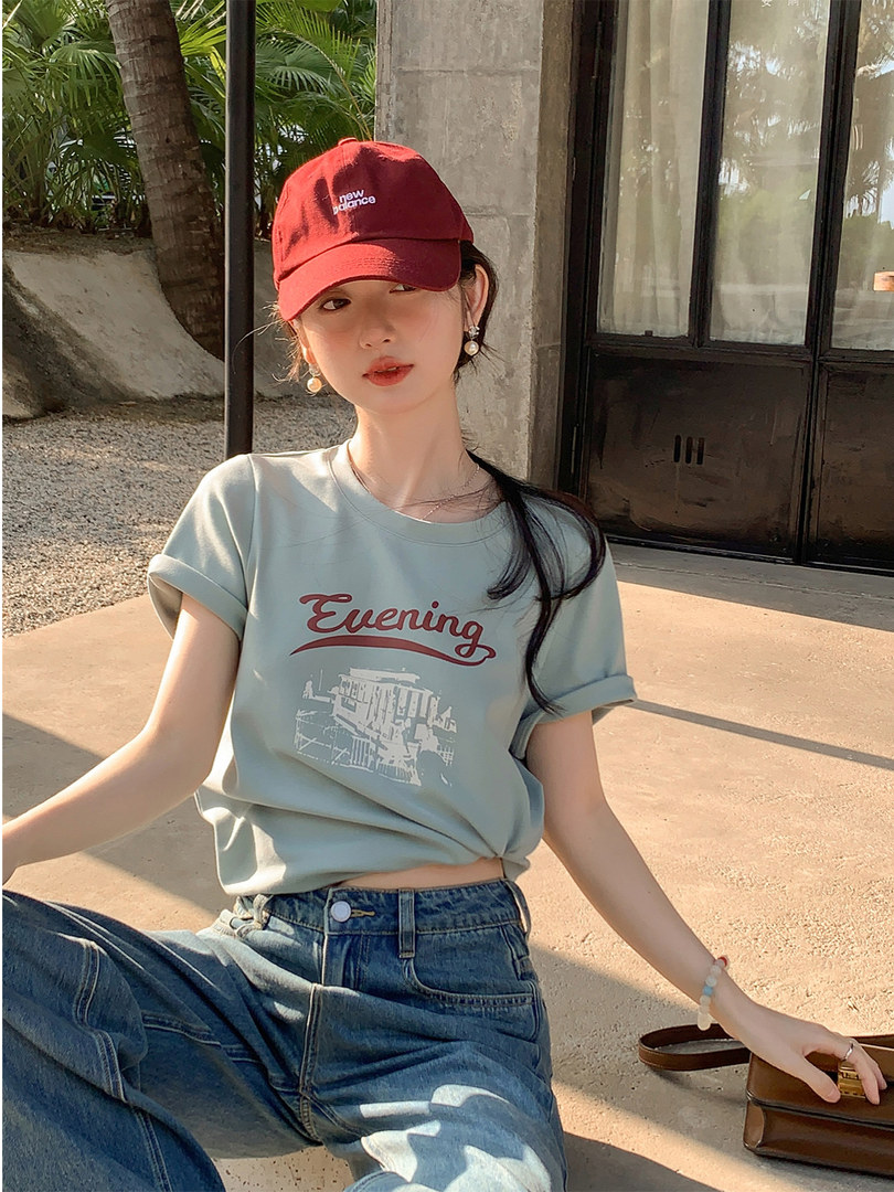 Woman wearing a light blue graphic T-shirt with jeans and a red cap outdoors