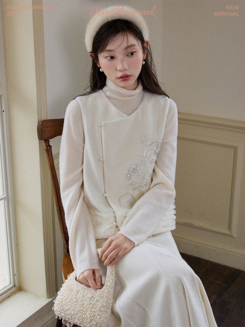Model wearing a cream winter outfit with a pearl beaded handbag