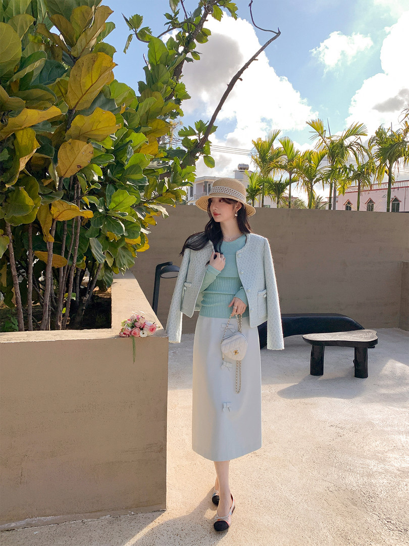 Woman modeling a light pastel outfit with a cropped jacket, knit top, midi skirt, and straw hat outdoors