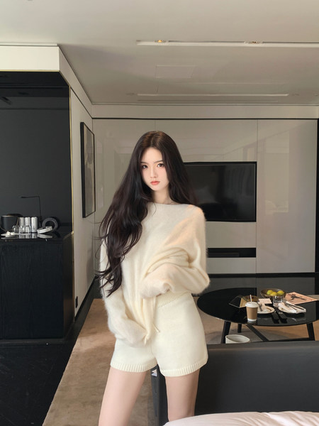 Model wearing a cream-colored knit sweater and matching shorts in a modern room setting