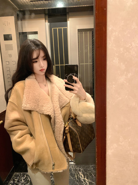 Woman taking mirror selfie wearing a beige shearling jacket and carrying a designer handbag