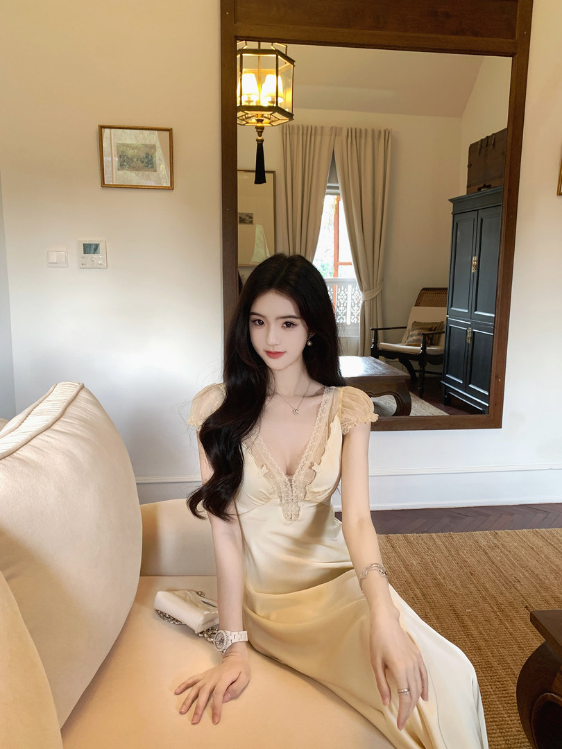 Woman wearing a cream-colored satin dress with lace detailing, sitting on a beige sofa.