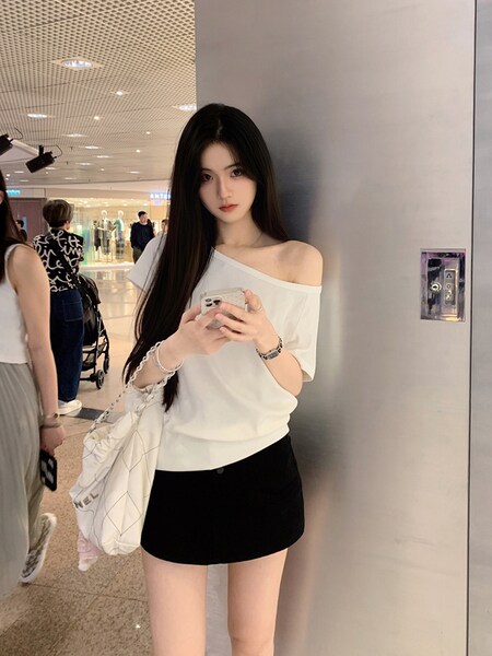 Woman wearing white off-shoulder top and black mini skirt in a mall setting