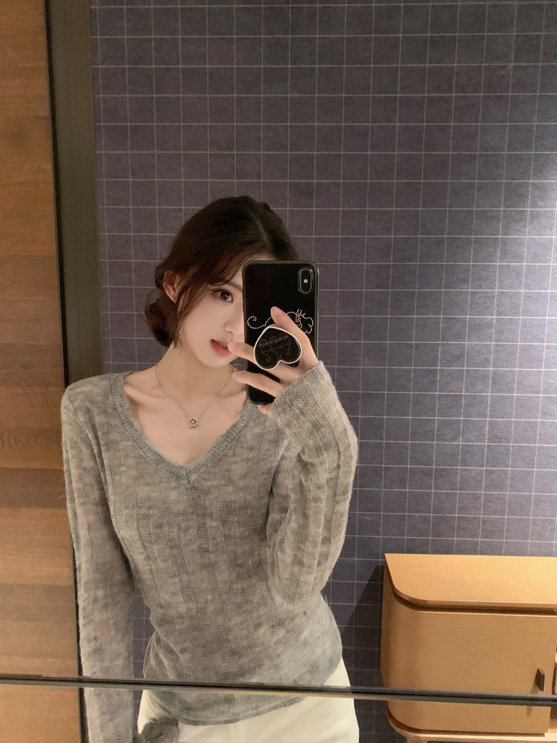 Woman taking mirror selfie wearing a gray V-neck sweater