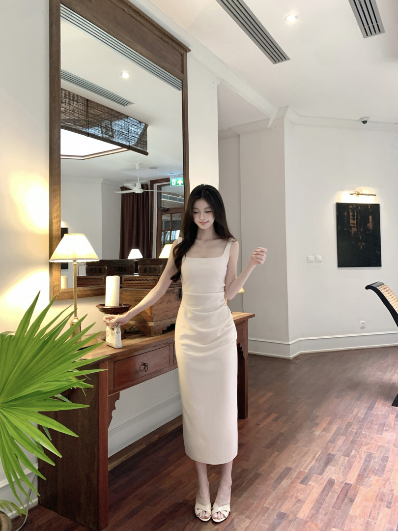 Woman wearing a cream-colored sleeveless midi dress in a well-lit indoor setting