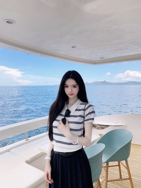 Woman wearing striped polo shirt and black pleated skirt on a yacht