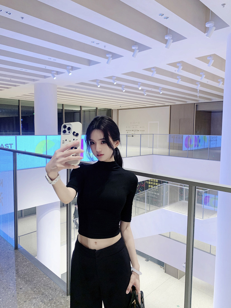 Woman taking mirror selfie wearing black crop top and black pants in a modern indoor space