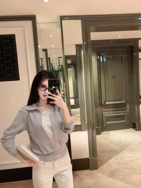 Woman taking mirror selfie wearing gray cardigan over white top and white pants