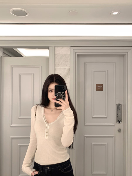 Woman taking mirror selfie wearing cream long-sleeve top with buttons and dark jeans