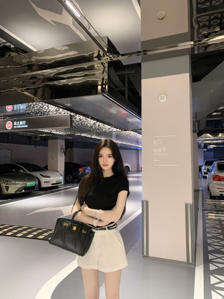 Woman wearing black top and white shorts holding a black handbag in a parking garage