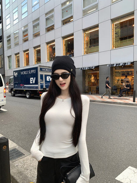 Woman wearing a white long-sleeve top, black beanie, and sunglasses on a city street