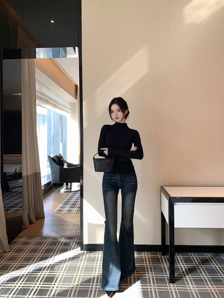 Woman wearing black turtleneck and flared jeans, holding a black quilted handbag.