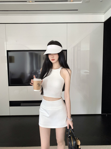Model wearing a white sleeveless crop top and matching mini skirt, holding a drink and handbag