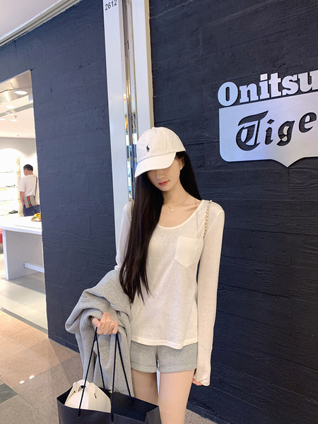 Woman wearing white long-sleeve top, gray shorts, and white cap, holding a shopping bag.