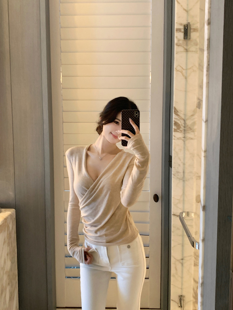 Woman wearing a beige wrap top with white pants in a mirror selfie