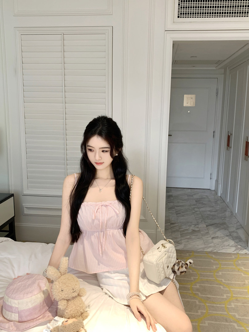 Woman wearing a pink striped top and white shorts, sitting on a bed with accessories.