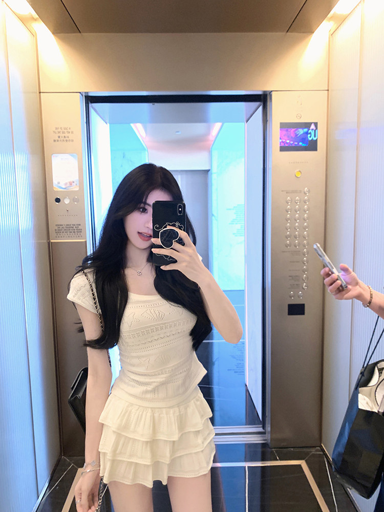 Woman taking a mirror selfie in an elevator wearing a cream-colored ruffled dress.
