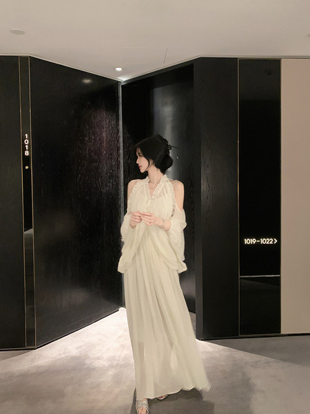 Woman wearing a white off-shoulder long dress with ruffled details, standing in a modern hallway.