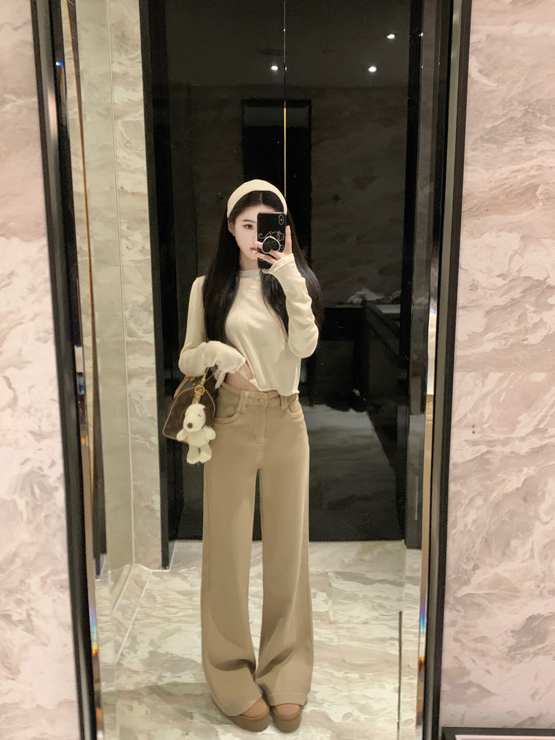 Woman taking mirror selfie wearing beige top, wide-leg pants, and headband with a small bag.